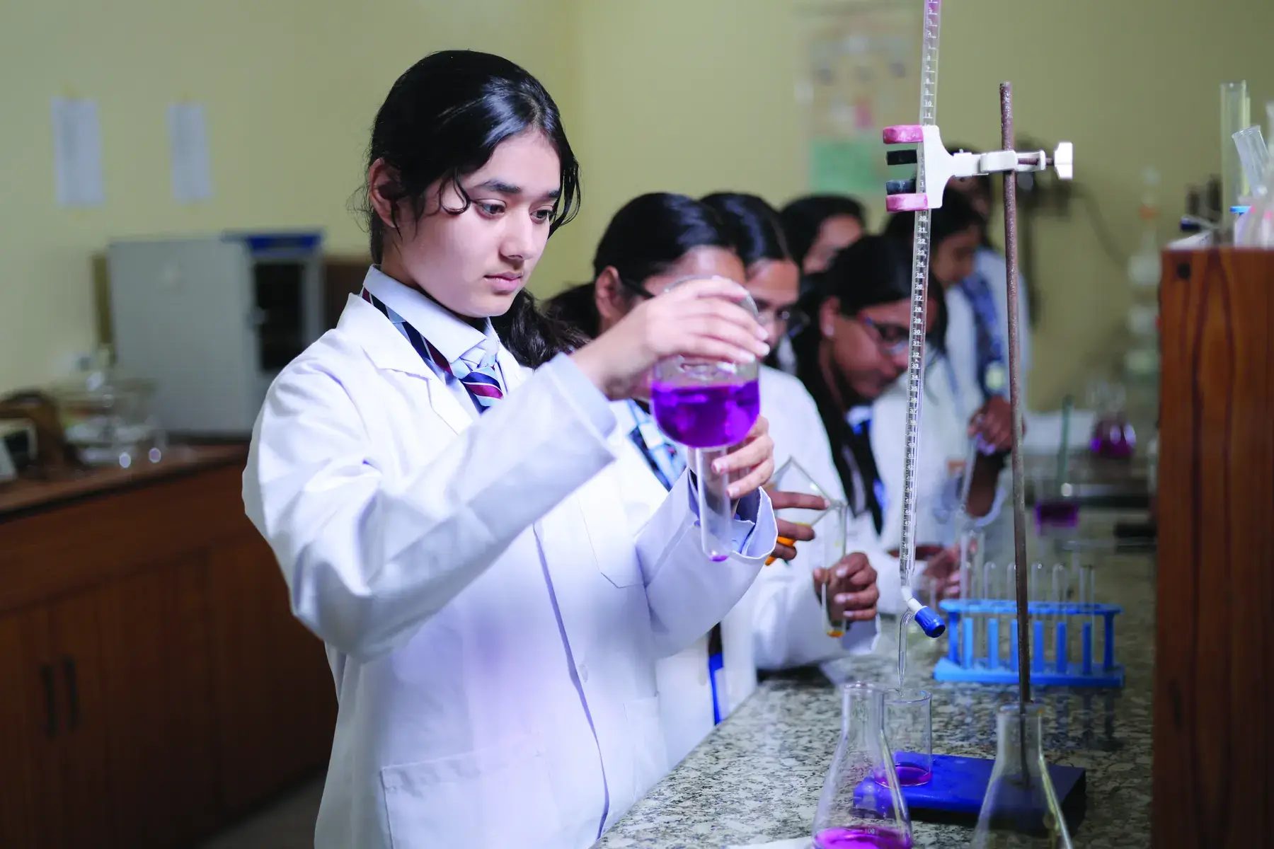 A student in a lab coat pouring a solution during a titration